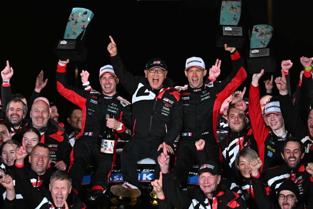 Sebastien Ogier (top center R) and his co-driver Vincent Landais (top center L) of France celebrate their victory with Toyota Gazoo Racing chairman Akio Toyoda (top C) and other team officers during the podium ceremony of the Rally Japan, the 13th round of the FIA World Rally Championships, in Toyota city, Aichi prefecture on November 9, 2025. (Photo by Toshifumi KITAMURA / AFP)