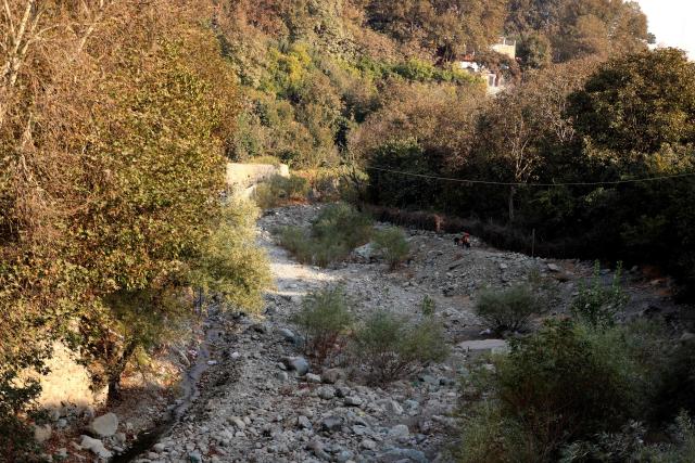 A family stand on the banks of the dried-up Kan River, west of Tehran on November 9, 2025, as the Iran faces sever water shortages. Iran was laying plans on November 8, 2025, to cut off water supplies periodically to Tehran's 10-million-strong population as it battles its worst drought in many decades. (Photo by ATTA KENARE / AFP)
