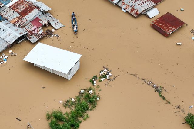 This aerial photo shows a resident paddles his boat in the flood waters past inundated houses in Tuguegarao City, Cagayan province, north of Manila on November 10, 2025, after a river overflowed following heavy rains brought about by Super Typhoon Fung-wong. A weakening Typhoon Fung-wong departed the Philippines over the South China Sea on the morning of November 10, after its driving winds and heavy rain killed at least two people and forced more than a million to evacuate. (Photo by John DIMAIN / AFP)