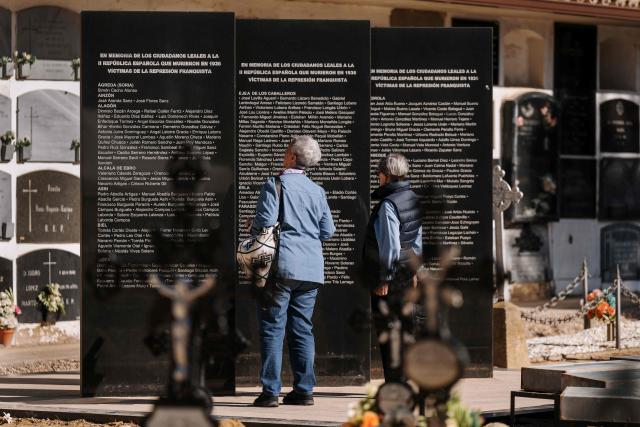 Relatives of the victims of repression during the Spanish Civil War and the Franco regime look at the names written on the monument that honors 417 dead in the cemetery of Ejea de los Caballeros, Ejea de los Caballeros, in Zaragoza province, on October 28, 2025. The monument made of three black stone monoliths was inaugurated in 2008 next to the mass grave, an initiative from the Ejea town council to honor the memory of those killed between July and October 1936. The Government of Aragon declared this space a Place of Democratic Memory in 2022, also honoring the victims of Nazi concentration camps. (Photo by Cesar MANSO / AFP)