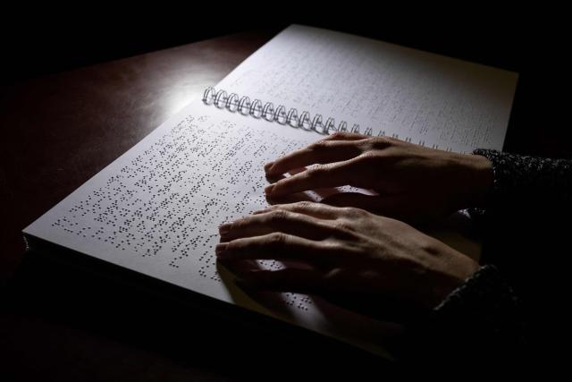 (FILES) A woman reads a book written in braille at the Centre for Braille Transcription and Editing (CTEB), the main braille publishing and printing house and bookshop in France, in Toulouse, southwestern France, on January 3, 2023, on the eve of World Braille Day. Celebrating its 200th anniversary, the Braille, an universal alphabet is fighting for its survival as its defenders warn of the risk of illiteracy among the visually impaired if nothing is done to reverse the trend. (Photo by Lionel BONAVENTURE / AFP)