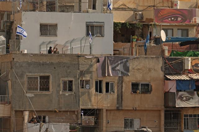 Israeli settlers place the Israeli flags on the roof of the Shweiki family house, after the Palestinian family was evicted by police from the house they lived in for decades, in east Jerusalem predominantly Arab neighbourhood of Silwan, on November 10, 2025. The eviction comes amid a decades-long legal battle between hundreds of Palestinian residents and an Israeli nonprofit, which claims the land under a 1970s law allowing Jews to reclaim property in East Jerusalem - rights not extended to Palestinians who were forced to abandon property in the cities. (Photo by AHMAD GHARABLI / AFP)