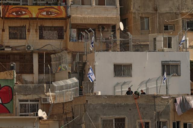 Israeli settlers place the Israeli flags on the roof of the Shweiki family house, after the Palestinian family was evicted by police from the house they lived in for decades, in east Jerusalem predominantly Arab neighbourhood of Silwan, on November 10, 2025. The eviction comes amid a decades-long legal battle between hundreds of Palestinian residents and an Israeli nonprofit, which claims the land under a 1970s law allowing Jews to reclaim property in East Jerusalem - rights not extended to Palestinians who were forced to abandon property in the cities. (Photo by AHMAD GHARABLI / AFP)