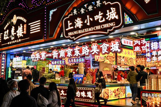 People walk past shops selling food on a pedestrian street in the Huangpu district in Shanghai on November 10, 2025. (Photo by Hector RETAMAL / AFP)