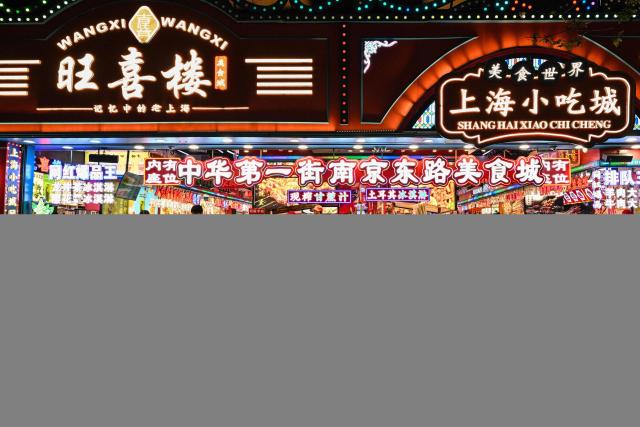 People walk past shops selling food on a pedestrian street in the Huangpu district in Shanghai on November 10, 2025. (Photo by Hector RETAMAL / AFP)