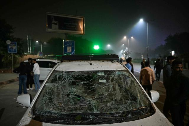 People gather beside a damaged vehicle at the blast site after an explosion near the Red Fort in the old quarters of Delhi on November 10, 2025. At least eight people were killed and 19 injured when a car exploded in the heart of the Indian capital on November 10, New Delhi's deputy fire chief told AFP. (Photo by Sajjad HUSSAIN / AFP)