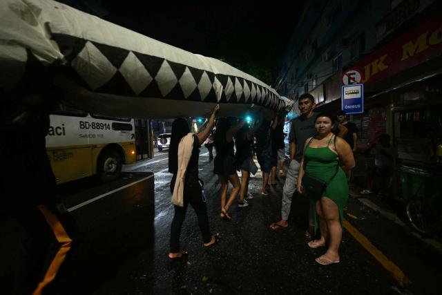 People at a bus stop watch activists carrying a snake-shaped puppet in Belem, Brazil, on November 10, 2025, during a protest organized by Oxfam Brazil and the Alliance of Peoples for Climate to mark the end of the first day of COP30. The COP30 runs from November 10 to 21, and the 50,000 participants will feel the heavy, humid air of the Amazon rainforest, and face the daunting task of keeping global climate cooperation from collapsing. (Photo by Mauro PIMENTEL / AFP)