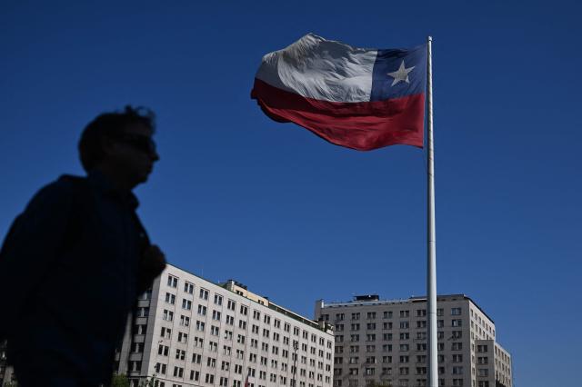 A man walks past a Chilean flag near La Moneda Presidential palace in Santiago on November 10, 2025. Chile will hold presidential election on November 16. (Photo by Marvin RECINOS / AFP)