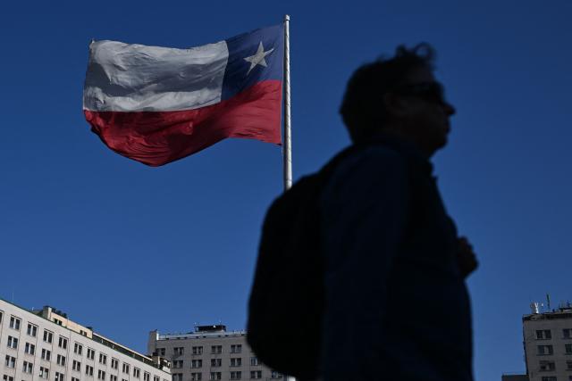 A man walks past a Chilean flag near La Moneda Presidential palace in Santiago on November 10, 2025. Chile will hold presidential election on November 16. (Photo by Marvin RECINOS / AFP)