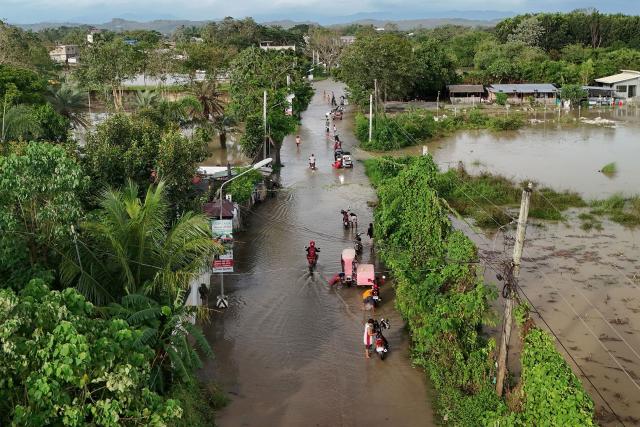 People wade through the water along a submerged street in Tuguegarao City, Cagayan province, north of Manila on November 11, 2025, as flood waters continue to inundate homes due to heavy rains brought about by Super Typhoon Fung-wong. Entire villages lay submerged and scores of towns remained without electricity on November 10 as Typhoon Fung-wong left the Philippines after killing at least five people and displacing more than a million. (Photo by John Dimain / AFP)