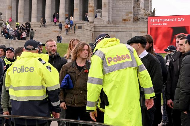 Police move members of the neo-Nazi National Socialist Network (NSN) after they unfurled a flag following a Remembrance Day service at Melbourne's Shrine of Remembrance on November 11, 2025. Each year on November 11 Australians mark Remembrance Day during which they observe a one minute's silence on the 11th hour of the 11th day of the 11th month to honour all who have served, suffered, or died in wars, conflicts, and peacekeeping operations. (Photo by William WEST / AFP)