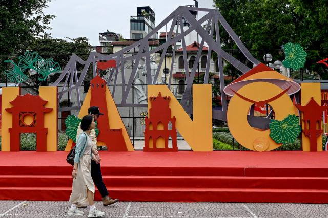 A couple walks past an installation spelling out the Hanoi city name with landmark symbols in Hanoi on November 11, 2025. (Photo by Nhac NGUYEN / AFP)