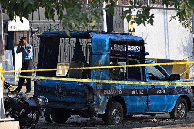 A policeman stands near the wreckage of a police vehicle at the cordoned-off site, a day after the suicide bombing, in Islamabad on November 12, 2025. Charred vehicles and a mangled motorcycle lay outside Islamabad's district court on November 11, their metal frames still warm as investigators sealed off the area where a suicide bomber had killed at least 12 people. (Photo by Aamir QURESHI / AFP)