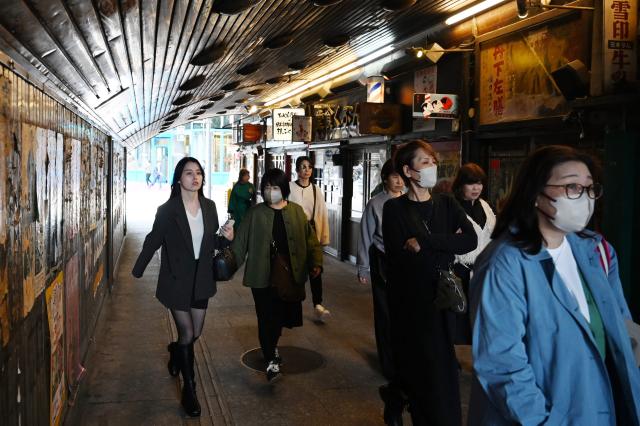People walk past restaurants below a bullet train track in Tokyo on November 12, 2025. (Photo by GREG BAKER / AFP)