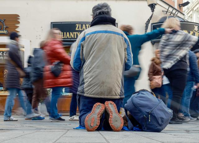 A group of people walk past a man begging for money in the old town in Bratislava, Slovakia on November 11, 2025. A new law to improve safety on pavements in Slovakia has prompted mockery and criticism, with claims that fleet-footed pedestrians could be caught speeding. The Slovak parliament approved a proposal to set a maximum speed limit for all pavement-users, from pedestrians to cyclists, skaters, scooter and e-scooter riders. But the agreed six kilometre (3.7-mile) per hour limit triggered bemusement online and a rash of memes about speeding pedestrians or whether they will need a licence to walk. Pavement users who exceed the limit could be fined up to 100 euros ($116), although it is not yet clear how police will implement the law when it comes into effect on January 1, 2026. (Photo by Joe Klamar / AFP)