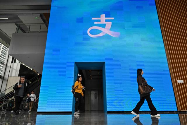 People arrive at the headquarters of Chinese digital payments platform Alipay in the Pudong district in Shanghai on November 12, 2025. (Photo by Hector RETAMAL / AFP)
