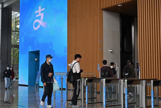 People arrive at the headquarters of Chinese digital payments platform Alipay in the Pudong district in Shanghai on November 12, 2025. (Photo by Hector RETAMAL / AFP)