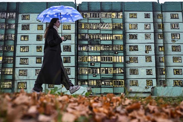 A woman passes by a graffiti of a typical Moscow suburb apartment building near Moscow's Kursky railway station on November 12, 2025. (Photo by Olesya KURPYAYEVA / AFP)