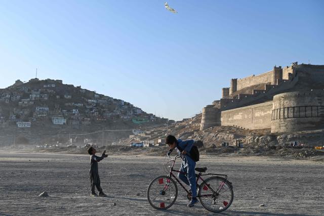 TOPSHOT - Afghan boys ride a bicycle and fly a kite near the Shuhada Lake in Kabul on November 12, 2025. (Photo by Wakil KOHSAR / AFP)