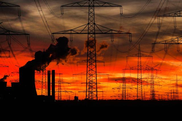 This picture taken at sunset on November 12, 2025 shows power poles near the lignite-fired power station (L) operated by German energy giant RWE near Niederaussem, western Germany. (Photo by Ina FASSBENDER / AFP)