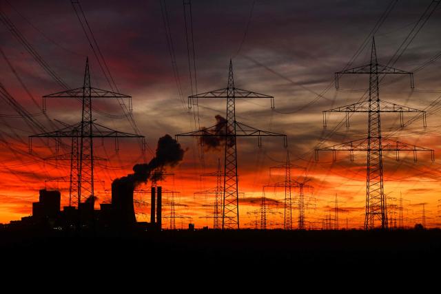 This picture taken at sunset on November 12, 2025 shows power poles near the lignite-fired power station (L) operated by German energy giant RWE near Niederaussem, western Germany. (Photo by Ina FASSBENDER / AFP)