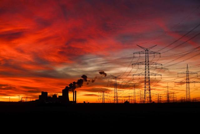 This picture taken at sunset on November 12, 2025 shows power poles near the lignite-fired power station (L) operated by German energy giant RWE near Niederaussem, western Germany. (Photo by Ina FASSBENDER / AFP)