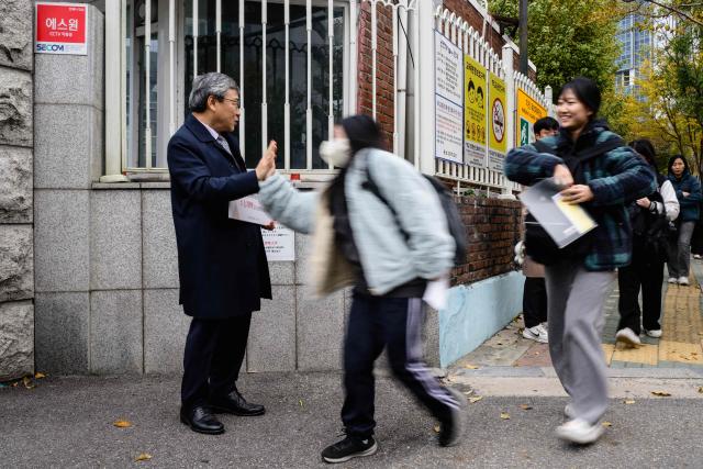Jung Keun-sik (L), superintendent of the Seoul Metropolitan Office of Education (SMOE), high fives students as they arrive for the annual college entrance exam, known locally as Suneung, outside the Gwangnam High School in Seoul on November 13, 2025. (Photo by ANTHONY WALLACE / AFP)