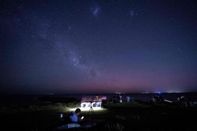 Star gazers gather to watch the Aurora Australis, also known as the Southern Lights, illuminating the night sky at Gerroa Headland in Kiama, around 133 kilometres south of Sydney, on November 13, 2025. (Photo by Saeed Khan / AFP)