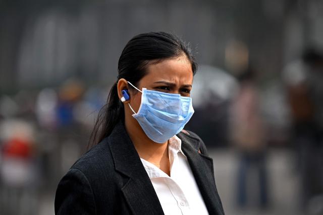 A woman wearing a face mask walks along a street amid smoggy conditions in New Delhi on November 13, 2025.  (Photo by Sajjad HUSSAIN / AFP)