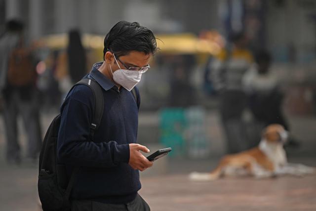 A man checks his smartphone as he walks along a street amid smoggy conditions in New Delhi on November 13, 2025.  (Photo by Sajjad HUSSAIN / AFP)