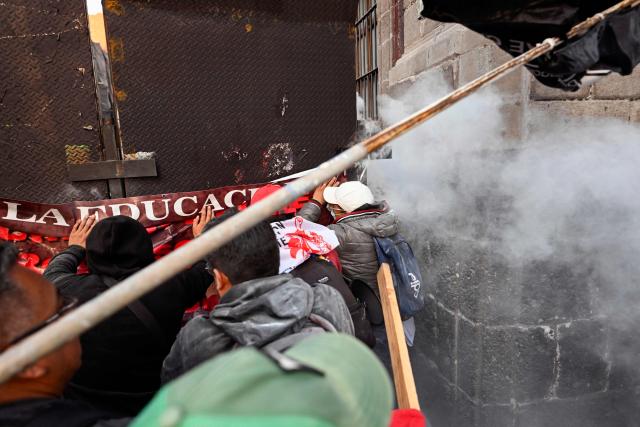 Men push against a security fence outside the National Palace during a protest, where Mexico's President Claudia Sheinbaum was located, in Mexico City on November 13, 2025. Teachers began a 48-hour work stoppage today to demand a salary increase (Photo by Alfredo ESTRELLA / AFP)