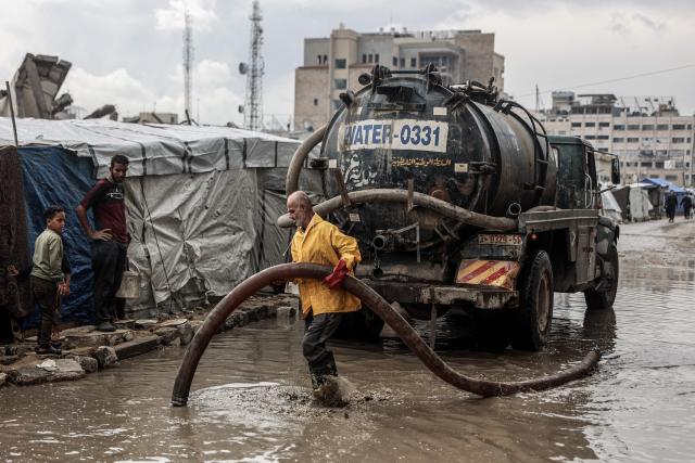 A Palestinian man clears stagnant water from the road near a displacement camp after the first winter rainfall in Gaza City on November 14, 2025. The United States on November 13 called on the UN Security Council to unite and back its draft resolution aimed at bolstering the US president's peace plan for Gaza, warning that Palestinians could otherwise suffer "grave" consequences. Last week, US officials launched negotiations within the Council on a draft that would follow up on the ceasefire in the two-year war between Israel and Hamas and endorse the plan. (Photo by Omar AL-QATTAA / AFP)