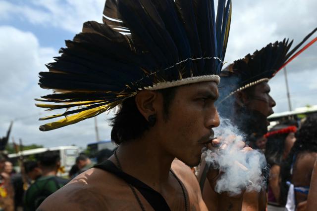 A Munduruku Indigenous man of the Ipereg Ayu movement smokes during a protest outside the COP30 UN Climate Change Conference, in Belem, Para State, Brazil, on November 14, 2025. (Photo by Mauro PIMENTEL / AFP)