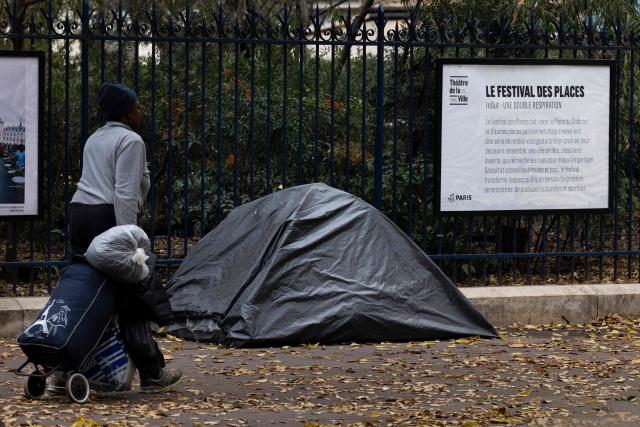 A homeless woman walks past a tent covered by a tarpaulin on a sidewalk in Paris on November 14, 2025. (Photo by JOEL SAGET / AFP)