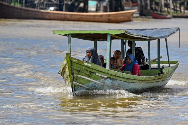 This picture taken on November 13, 2025 shows people commuting on a boat at a riverside village in Singkil, Indonesia's southern Aceh province. (Photo by CHAIDEER MAHYUDDIN / AFP)