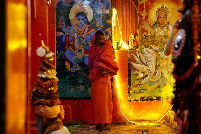 A man wearing a shawl stands in front of Hindu deities' murals at Dashashwamedh ghat along the banks of river Ganges in Varanasi on November 15, 2025. (Photo by Niharika KULKARNI / AFP)