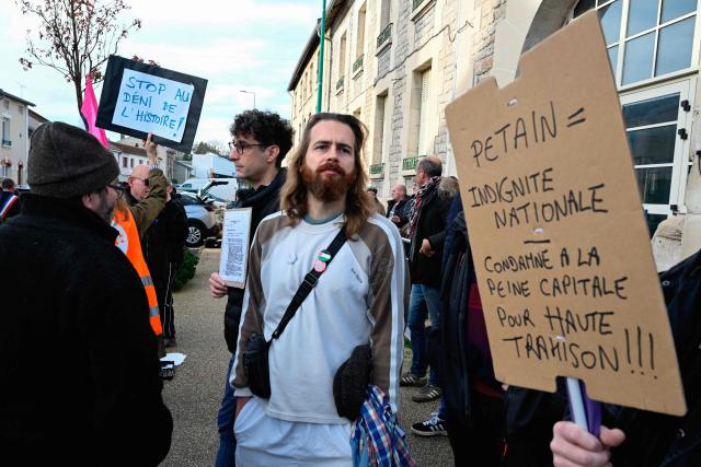 A demonstrator holds a placard reading "Petain = national indignity - sentenced to death for high treason !!!" during a protest in front of the Saint-Jean-Baptiste church, where takes place a religious ceremony "in homage to Marshal Pétain and his soldiers" organised by ADMP (Association to Defend the Memory of Marshal Petain) in Verdun, northeastern France on November 15, 2025. The administrative court authorized the religious ceremony the day before, ruling against the city's mayor who had banned it by decree. (Photo by Jean-Christophe VERHAEGEN / AFP)