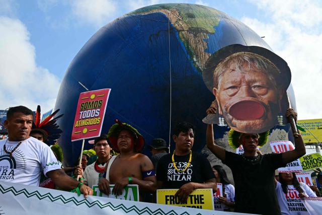 Indigenous people hold a sign reading "We are all affected" and another one depicting Brazilian Indigenous leader and activist Chief Raoni during the so-called "Great People's March" in the sidelines of the COP30 UN Climate Change Conference in Belem, Para State, Brazil on November 15, 2025. Thousands of people are expected to attend the march to demand "real solutions" to human-caused global warming , and which comes at the halfway point of contentious COP30 negotiations following two Indigenous-led protests that disrupted proceedings earlier in the week. (Photo by Pablo PORCIUNCULA / AFP)