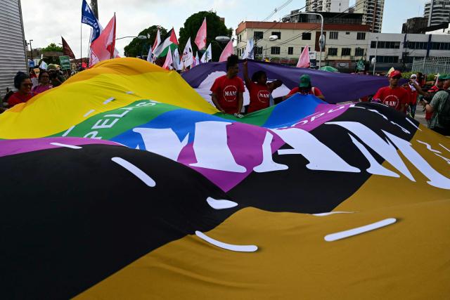 Members of the Movement for Popular Sovereignty in Mining (MAM) unfurl a huge flag during the so-called "Great People's March" in the sidelines of the COP30 UN Climate Change Conference in Belem, Para State, Brazil on November 15, 2025. Thousands of people are expected to attend the march to demand "real solutions" to human-caused global warming , and which comes at the halfway point of contentious COP30 negotiations following two Indigenous-led protests that disrupted proceedings earlier in the week. (Photo by Pablo PORCIUNCULA / AFP)