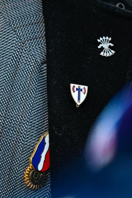 This photograph shows a close up of the jacket of Pierre-Nicolas Nups, member of Le Parti de la France, wearing pins of former French far-right party Front National (predecessor of  Rassemblement National (RN) party), of Vichy-regime era "Ordre de la Francisque" and of the fascist political organization Spanish Falange, as he speaks to the press during a religious ceremony at the Saint-Jean-Baptiste church in Verdun "in homage to Marshal Petain and his soldiers" in Verdun, northeastern France on November 15, 2025. The administrative court authorized the religious ceremony the day before, ruling against the city's mayor who had banned it by decree. (Photo by Jean-Christophe VERHAEGEN / AFP)
