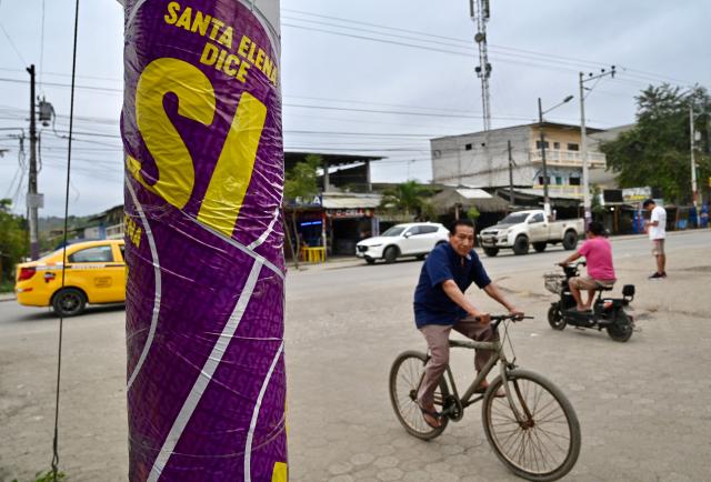 A man rides past a poster supporting the constitutional reform referendum in Olon on November 15, 2025. Ecuadorans will vote Sunday on whether to allow the return of foreign military bases and the drafting of a new constitution that could give the country's Trump-friendly president more power. (Photo by MARCOS PIN / AFP)