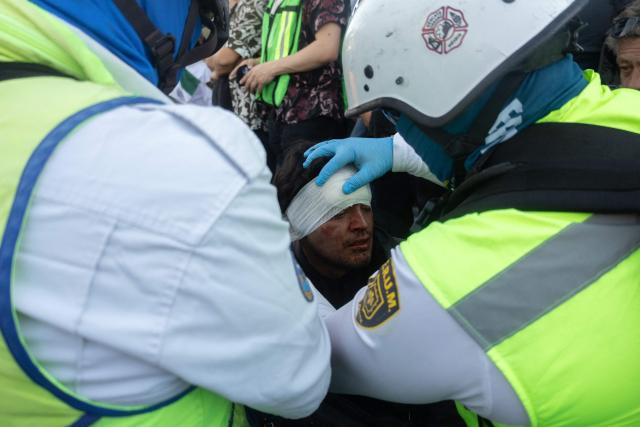 An injured demonstrator is helped by paramedics during clashes with riot police at a rally against the government of Mexico's President Claudia Sheinbaum at Zocalo Square in Mexico City on November 15, 2025. Thousands of people marched through the streets of Mexico City on Saturday to protest against drug violence and the security policies of President Claudia Sheinbaum's government. (Photo by Eva FONSECA / AFP)