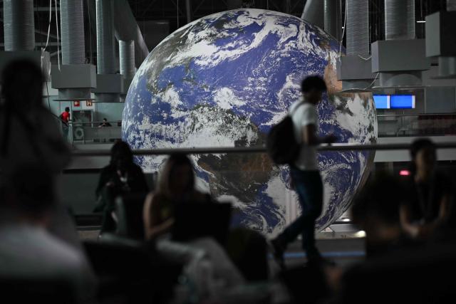 A man walks past a huge globe representing the earth hanged inside a ward for NGO's and civil and social associations, at the COP30 UN Climate Change Conference in Belem, Para State, Brazil on November 15, 2025. At the close of the first week of negotiations, Brazil’s COP30 presidency is expected to present a strategy to reconcile countries’ demands, focusing on strengthening climate goals and improving financial flows from wealthy to developing nations to boost resilience and support the transition to low-emission economies. (Photo by Mauro PIMENTEL / AFP)