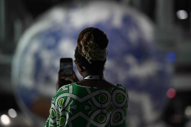 A woman takes a picture of a huge globe representing the earth hanged inside a ward for NGO's and civil and social associations, at the COP30 UN Climate Change Conference in Belem, Para State, Brazil on November 15, 2025. At the close of the first week of negotiations, Brazil’s COP30 presidency is expected to present a strategy to reconcile countries’ demands, focusing on strengthening climate goals and improving financial flows from wealthy to developing nations to boost resilience and support the transition to low-emission economies. (Photo by Mauro PIMENTEL / AFP)