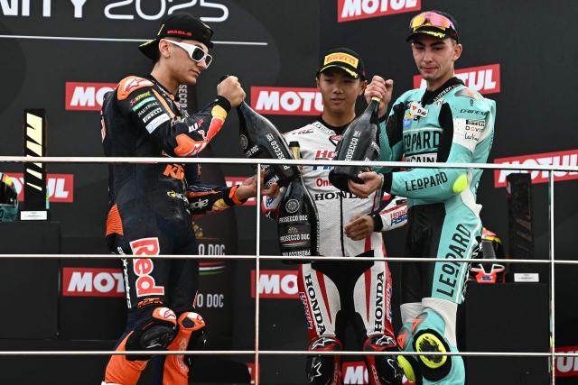 Second placed Red Bull KTM Tech3 team's Spanish Moto3 rider Alvaro Carpe (L), winner Leopard Raging team's Spanish Moto3 rider Adrian Fernandez (R) and third placed Honda Team Asia team's Japanese Moto3 rider Taiyo Furusato celebrate on the podium after the Moto3 race of the Valencia Grand Prix at the Ricardo Tormo racetrack in Cheste on November 15, 2025. (Photo by JOSE JORDAN / AFP)