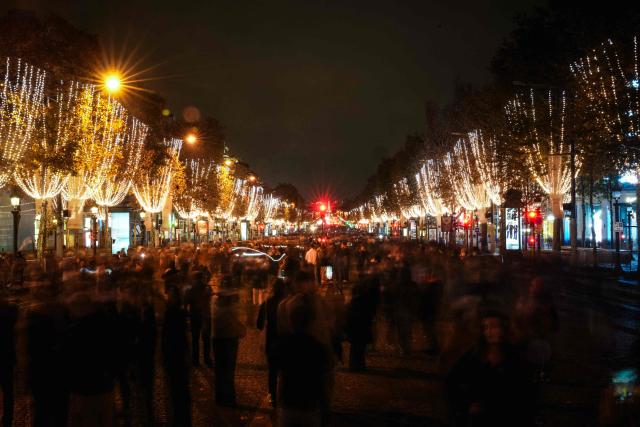 TOPSHOT - People walk along the Champs-Elysees avenue after the inauguration of the Christmas illuminations in Paris on November 16, 2025. (Photo by Dimitar DILKOFF / AFP)