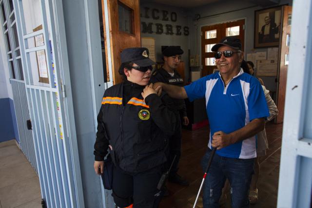 A blind man walks with the assistance of a Civil Defense of Chile officer during Chile's general election at a polling station in Antofagasta, Chile on November 16, 2025. Chileans are voting in a presidential election shaped by rising concerns over violent crime, with candidates pledging tougher measures against transnational gangs and the far-right promising to carry out mass migrant deportations. (Photo by SEBASTIAN ROJAS ROJO / AFP)