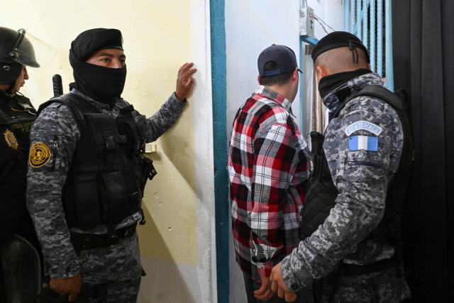 A Mara Salvatrucha gang member walks in the middle of prison guards during a raid at Pavoncito Prison in Fraijanes, Guatemala on November 17, 2025. The operation is part of measures announced by the new security authorities to regain control of the country's prisons following the October escape of 20 Barrio 18 gang leaders from Fraijanes II Prison, adjacent to Pavoncito. (Photo by JOHAN ORDONEZ / AFP)