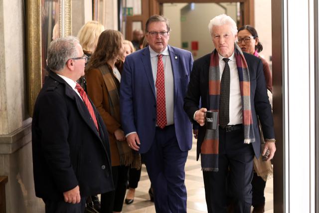 US actor Richard Gere (R) walks to the House of Commons after meeting with Members of Parliament in Ottawa, Canada on November 17, 2025, holding a mug from the Canadian television news program "Power & Politics," on the day of the final vote on the state budget. Canada's Liberal government survived a confidence vote on November 17, as parliament narrowly passed a budget Prime Minister Mark Carney says is essential to bolster an economy threatened by US tariffs. 
The minority Liberal government faced collapse over the cliffhanger budget vote, but a small group of opposition lawmakers -- weary of triggering a snap election -- allowed the fiscal plan to pass. (Photo by Dave Chan / AFP)