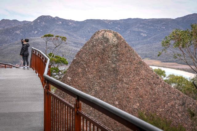 This picture taken on November 5, 2025 shows a tourist taking a photograph at a lookout located above Wineglass Bay at Freycinet Peninsula in Tasmania’s Freycinet National Park. (Photo by DAVID GRAY / AFP)